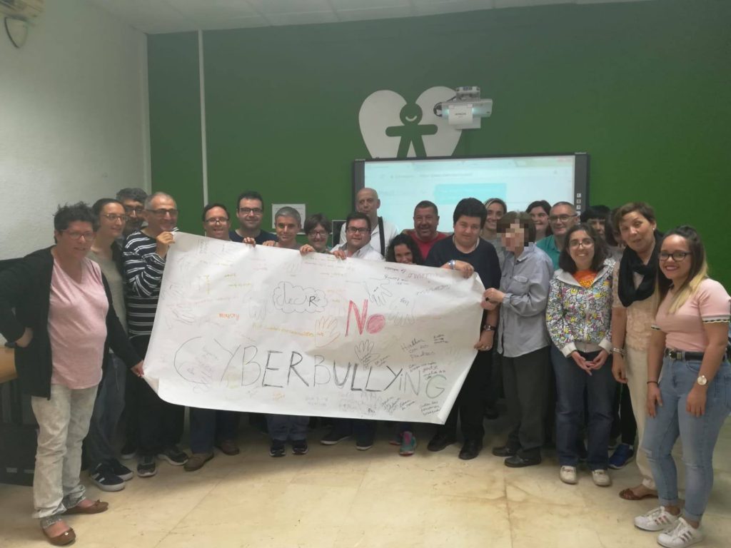 Imagen de participantes de la charla dirigida a socios y socias de la entidad mostrando la pancarta que realizaron con el texto central de "NO, al cyberbullying"