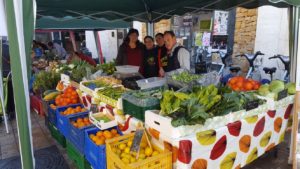 Imagen de 3 integrantes de la alquería durante en el puesto de un mercado con sus verduras y frutas ecológicas 