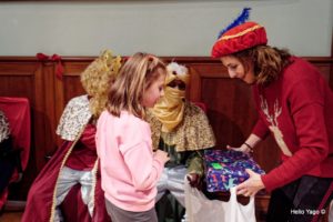 Niña recogiendo junto a los reyes magos en la fiesta de reyes de la asociación Amigos de la calle.